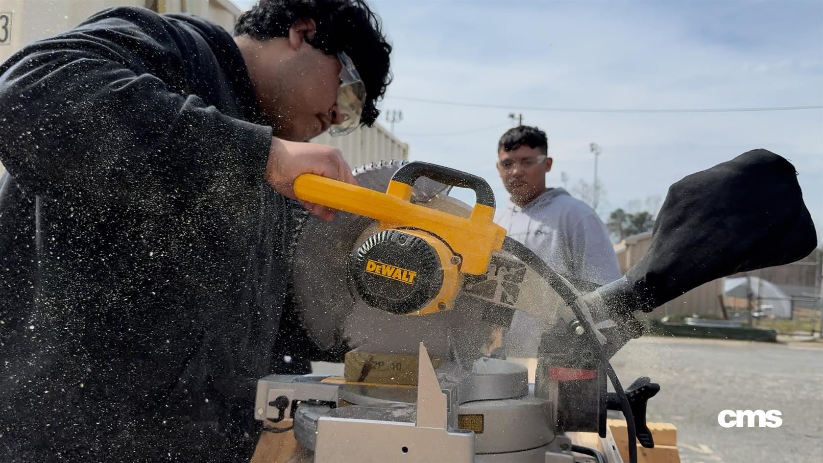  carpentry students cut through a 2x4 with a miter saw